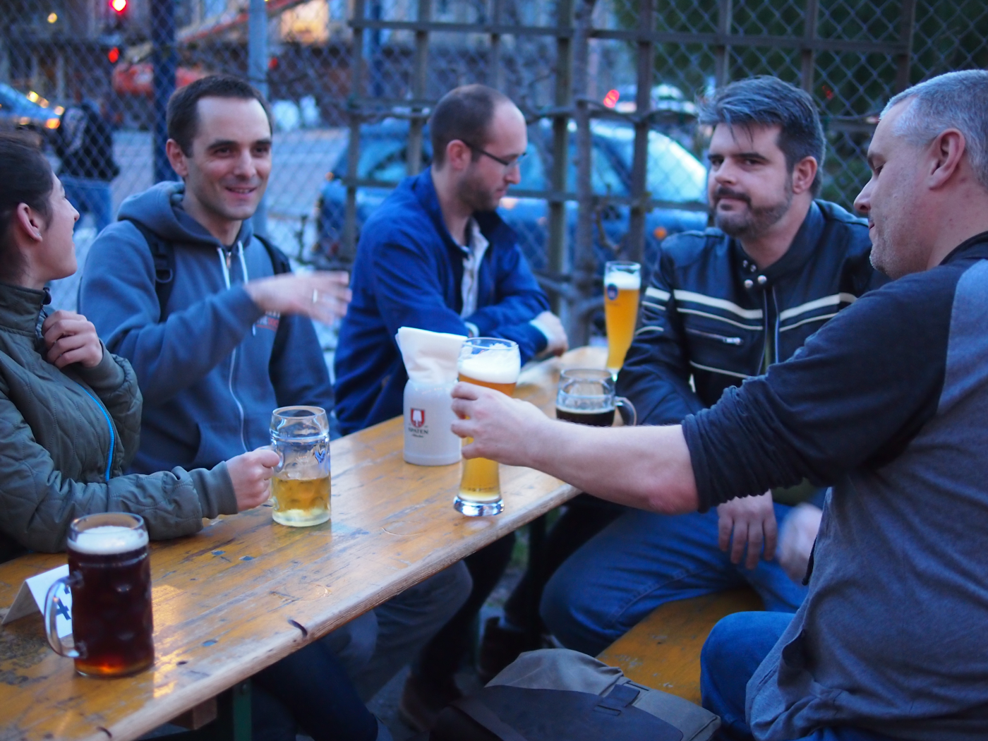 I and four people sit around a wooden picnic style table at a beer garden in SF. The blue grey tones and warm clothes indicate it&rsquo;s chilly outside. Folks have big classes full of beer and are engaged in conversation. One member of the group has spied the photographer and looks suspiciously at the camera.